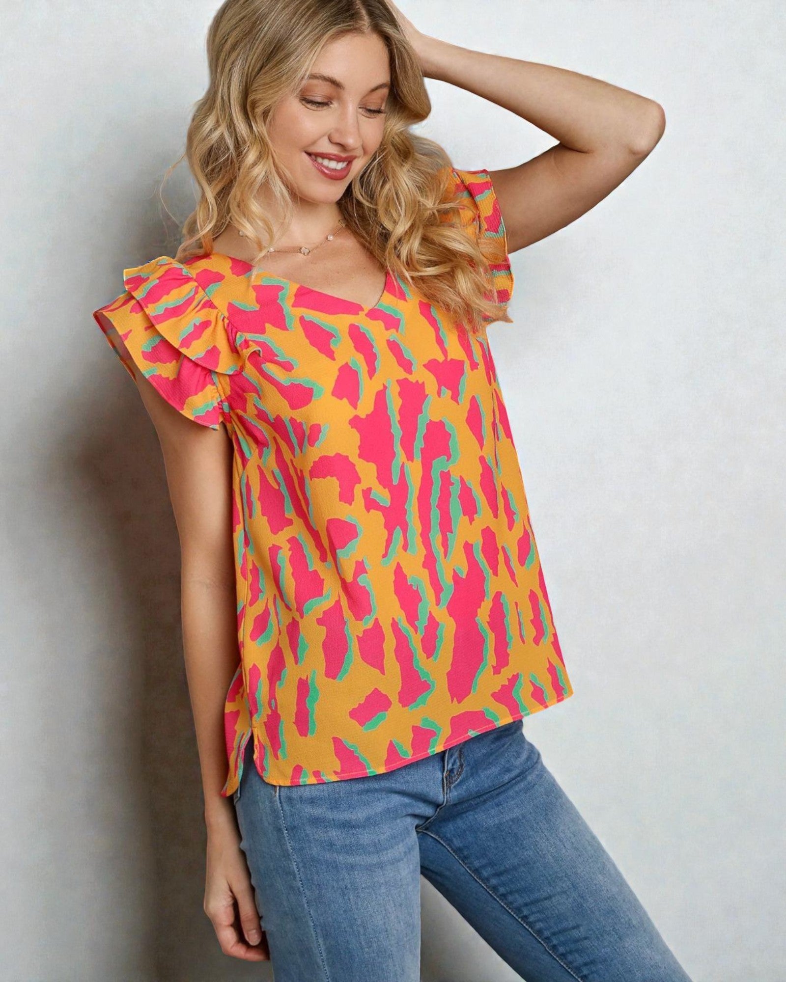 Woman wearing a colorful patterned top and blue jeans against a plain background