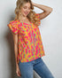 Woman wearing a colorful patterned top and blue jeans against a plain background