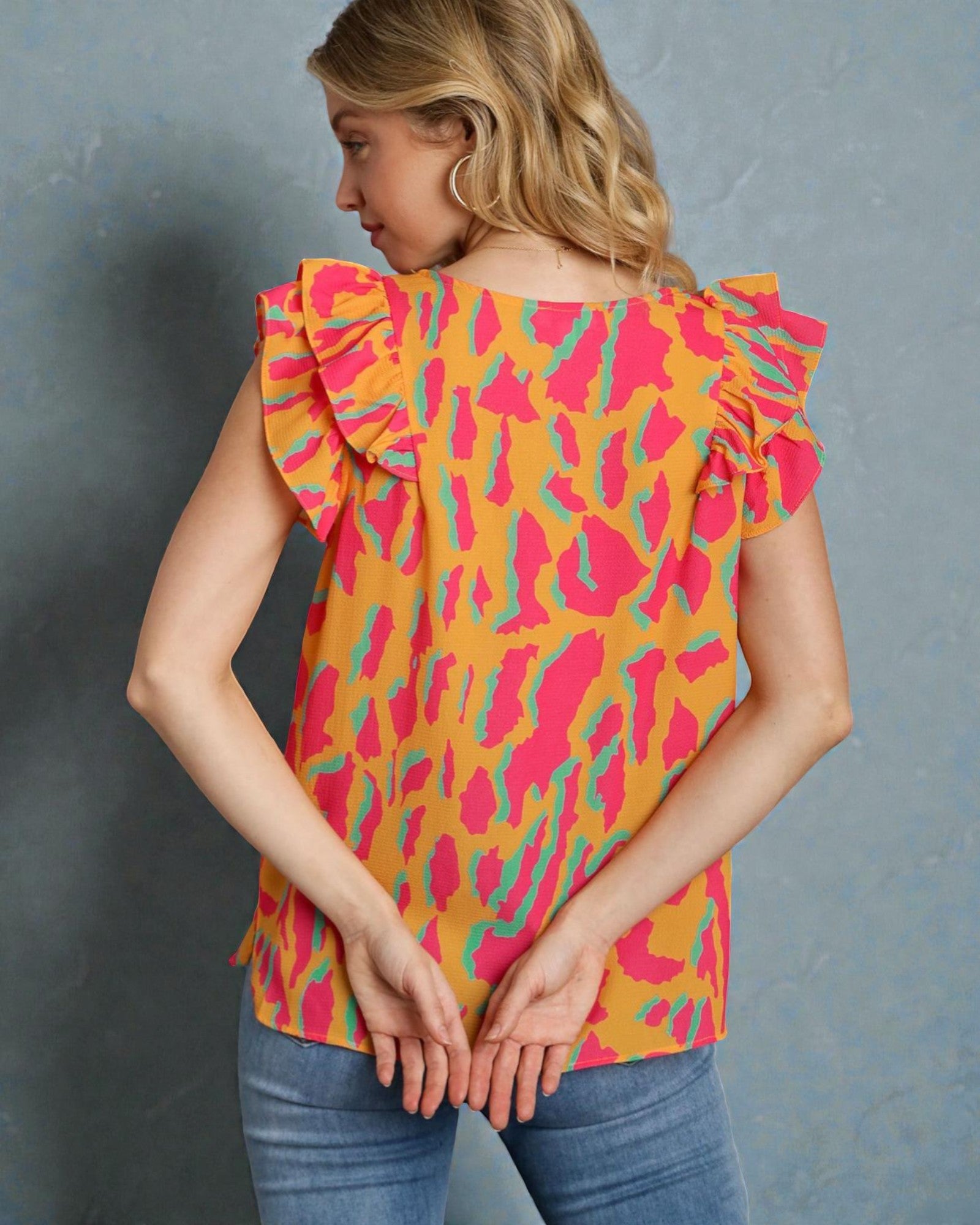 Woman wearing a colorful top with ruffled sleeves against a gray background