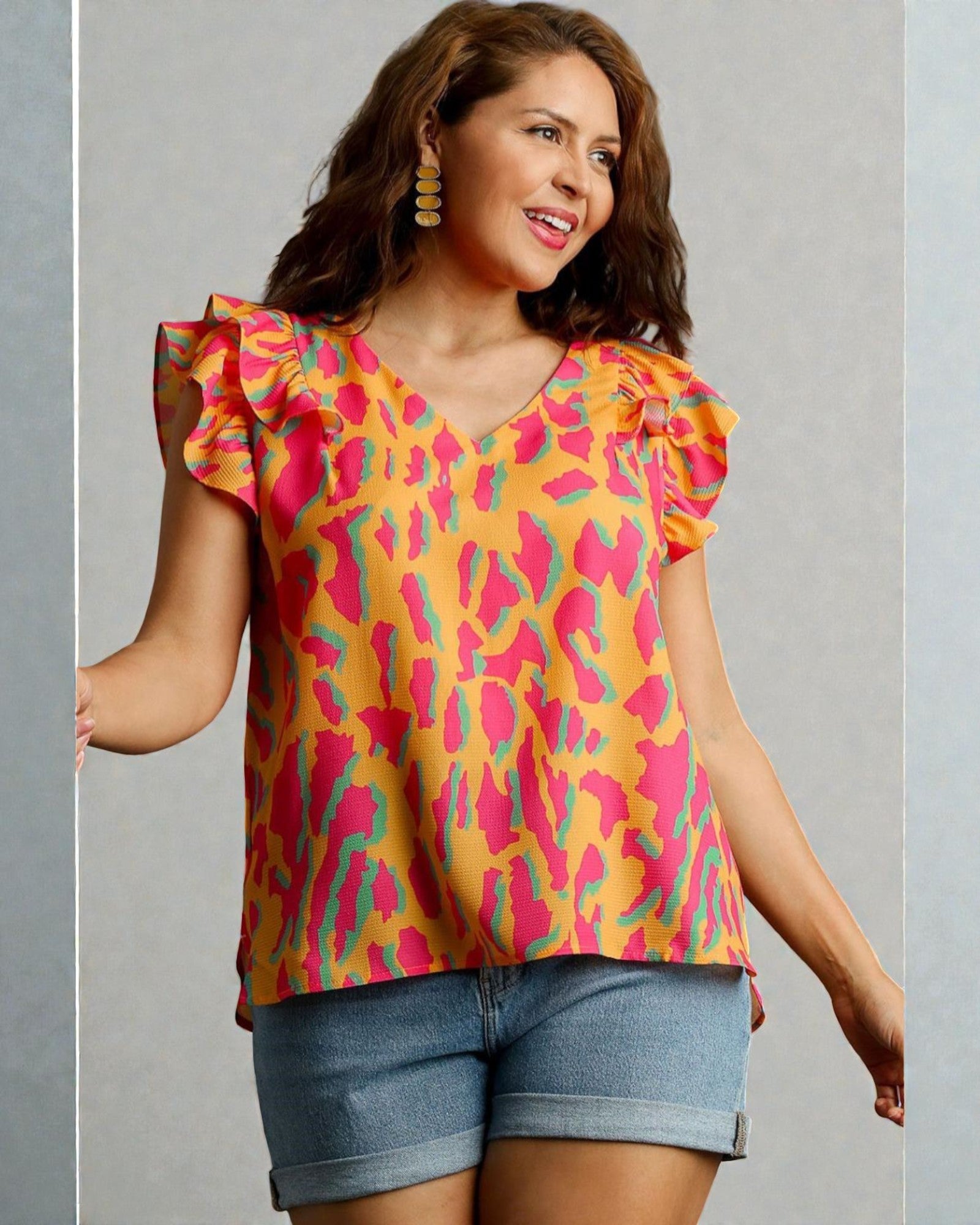 Woman wearing a colorful patterned top with ruffled sleeves on a gray background