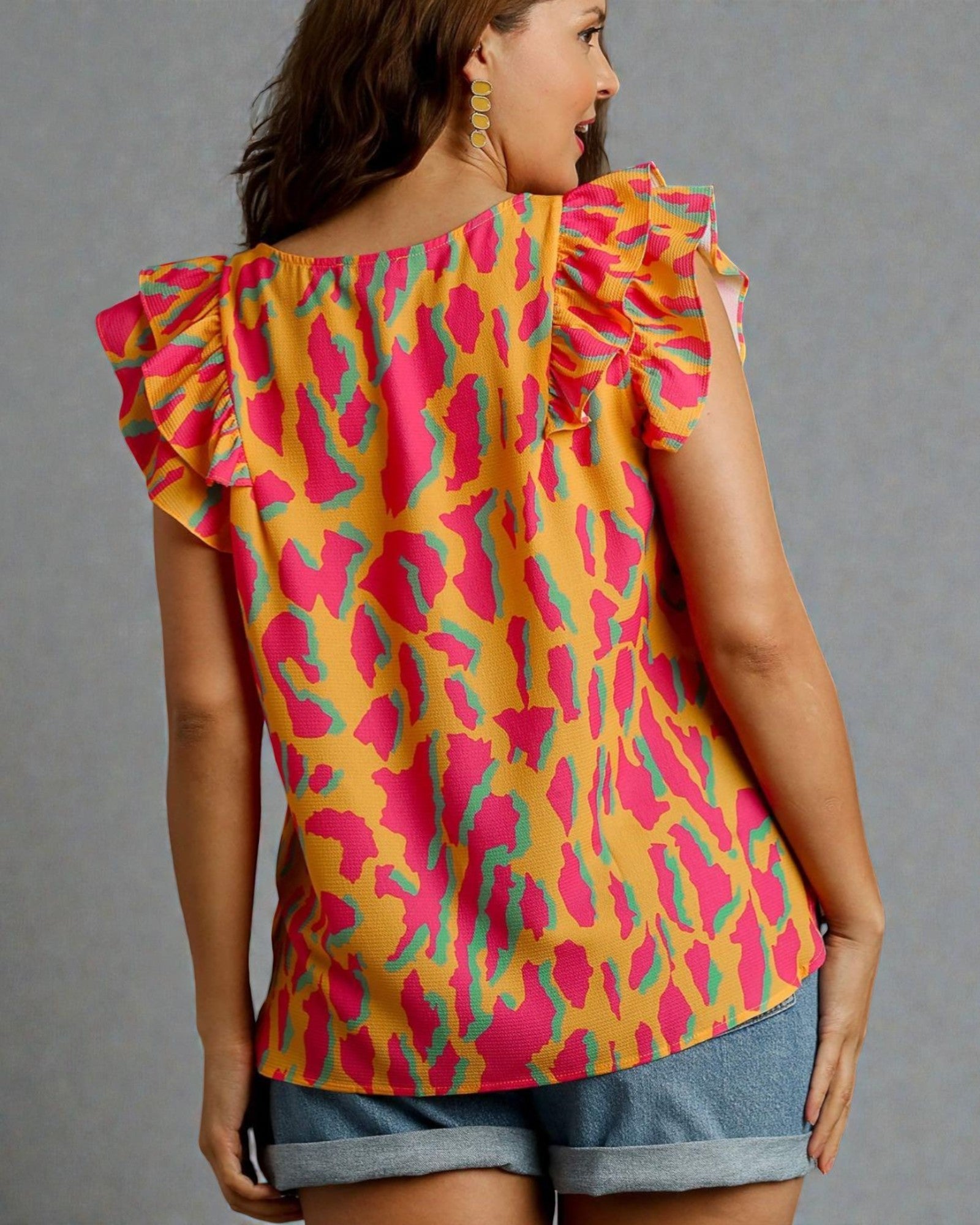 Woman wearing a colorful patterned top with ruffled shoulders on a gray background