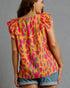 Woman wearing a colorful patterned top with ruffled shoulders on a gray background