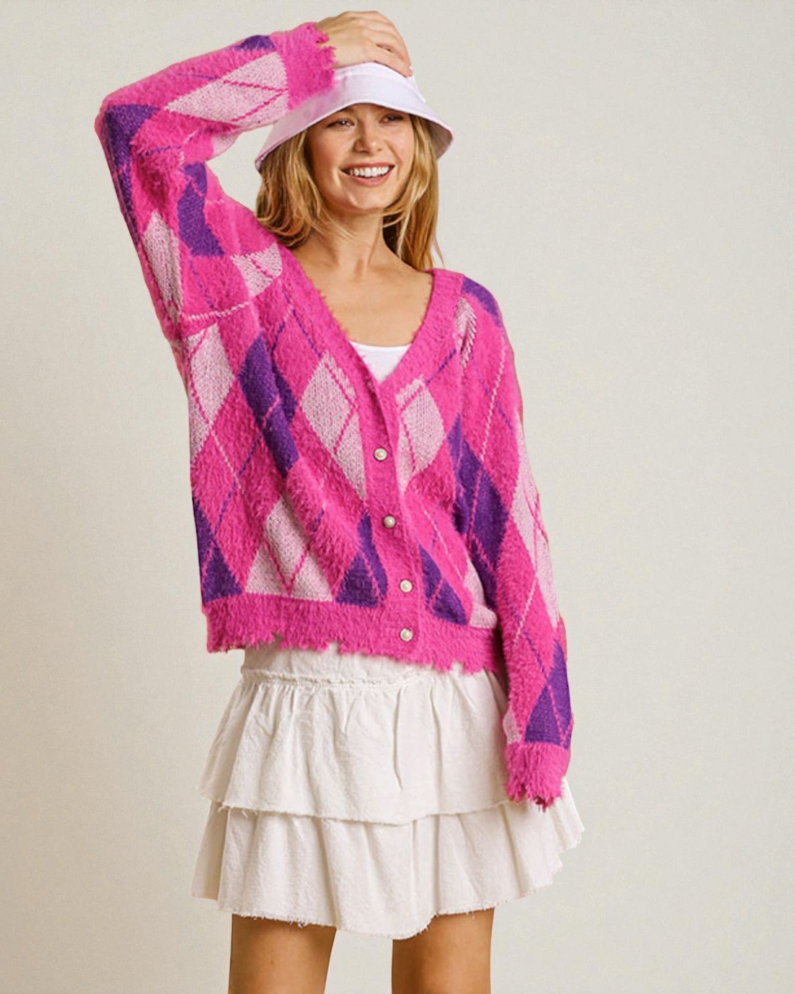 Woman wearing a pink and purple argyle cardigan with a white skirt on a plain background