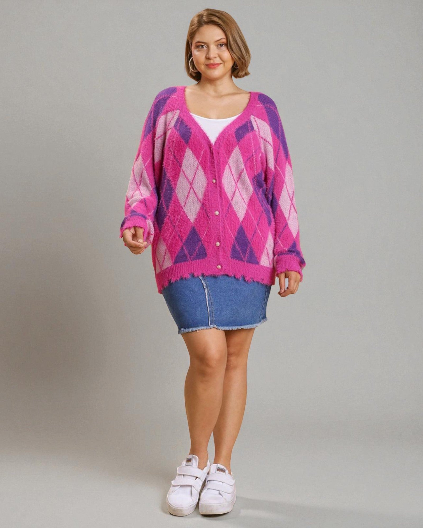 Woman wearing a pink argyle cardigan, denim skirt, and white sneakers on a gray background