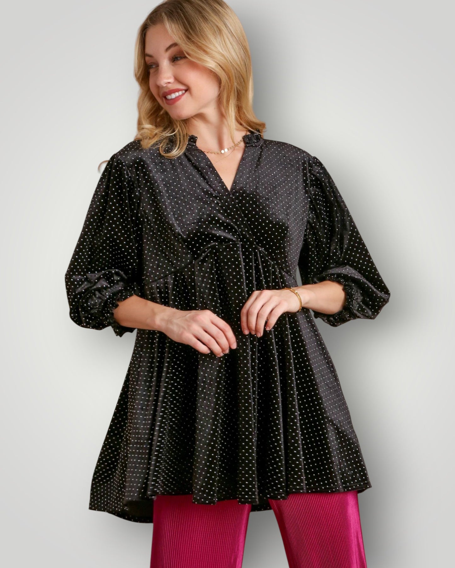 Woman wearing a black polka dot dress with pink pants on a plain background