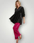 Woman wearing a black patterned top and pink pants on a white background