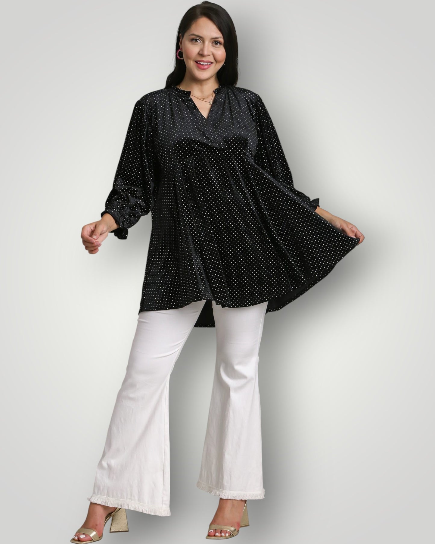 Woman wearing a black patterned top and white pants on a light gray background