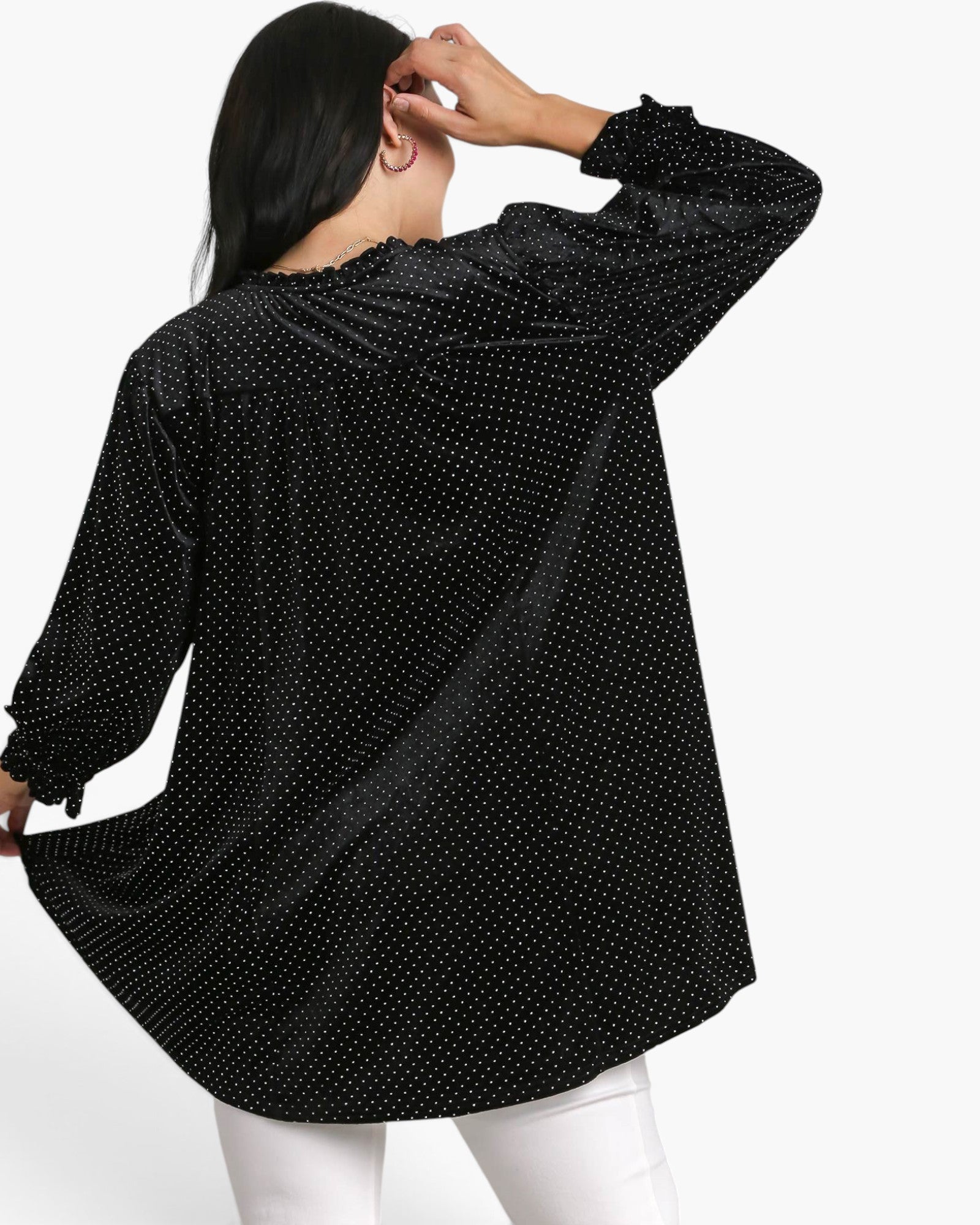 A woman shown from the back wearing a black long-sleeve blouse with a small white polka dot pattern and white pants, set against a plain white studio background.