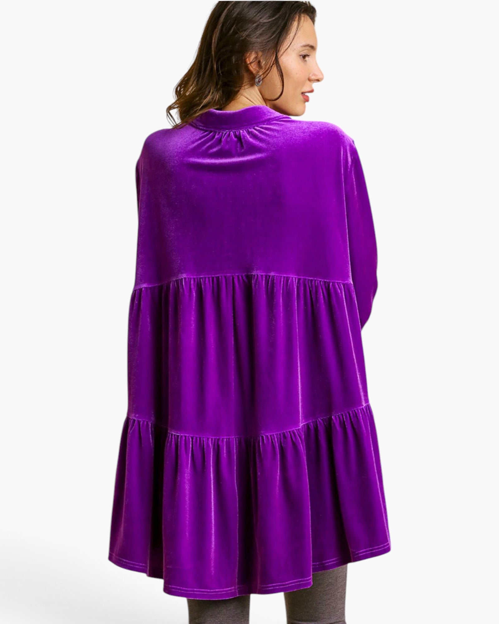A woman shown from the back wearing a bright purple velvet tiered cape-style dress against a plain light gray studio background.