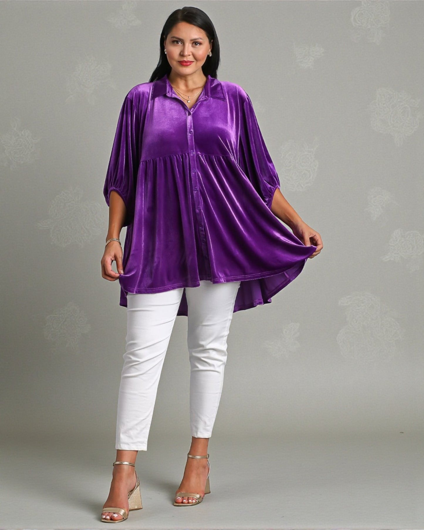 Woman wearing a purple top and white pants on a gray background