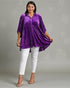 Woman wearing a purple top and white pants on a gray background