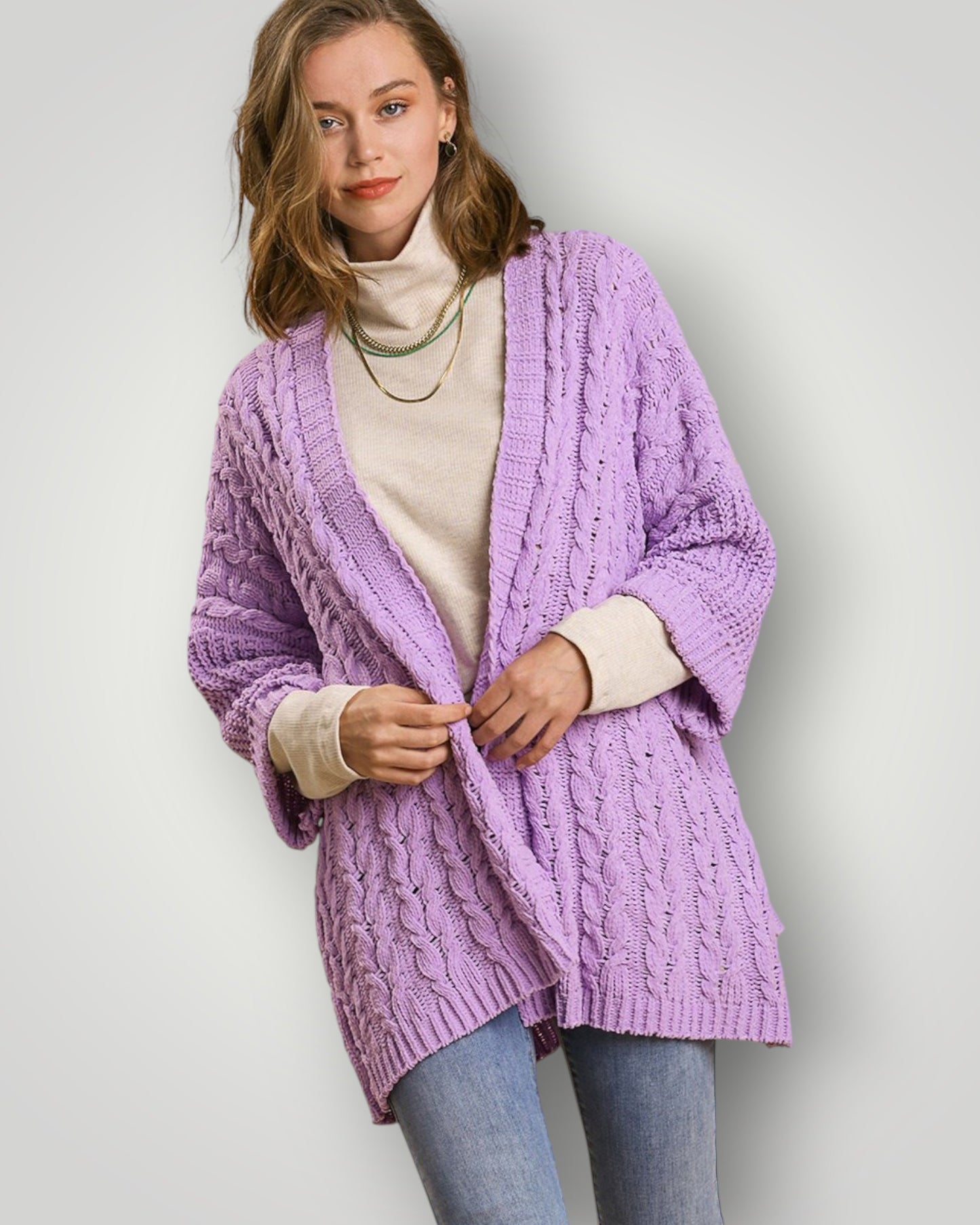 Woman wearing a purple cable knit cardigan over a white turtleneck on a plain background