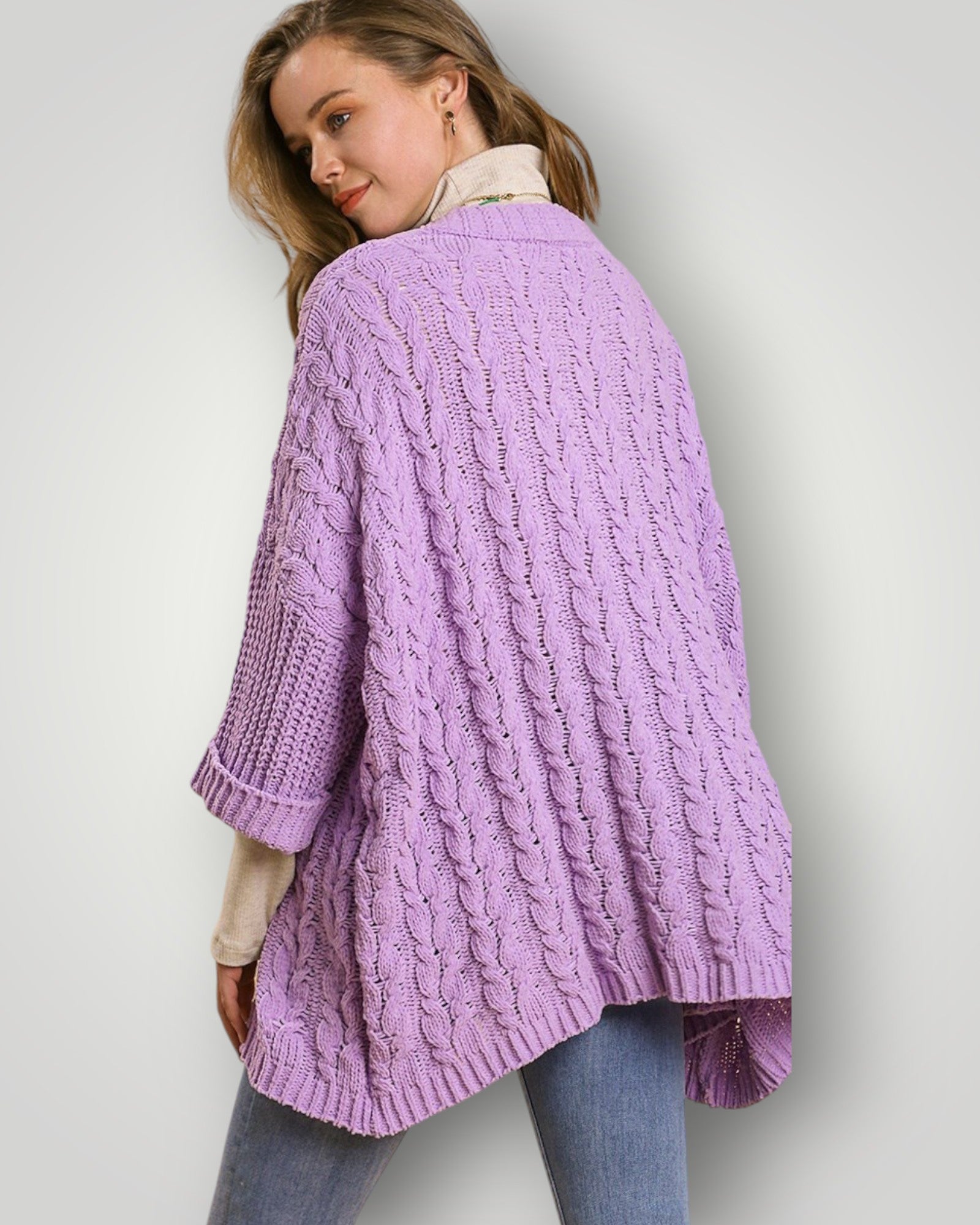 Woman wearing a purple cable knit cardigan on a plain background
