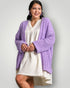 Woman wearing a purple cardigan over a white dress on a plain background