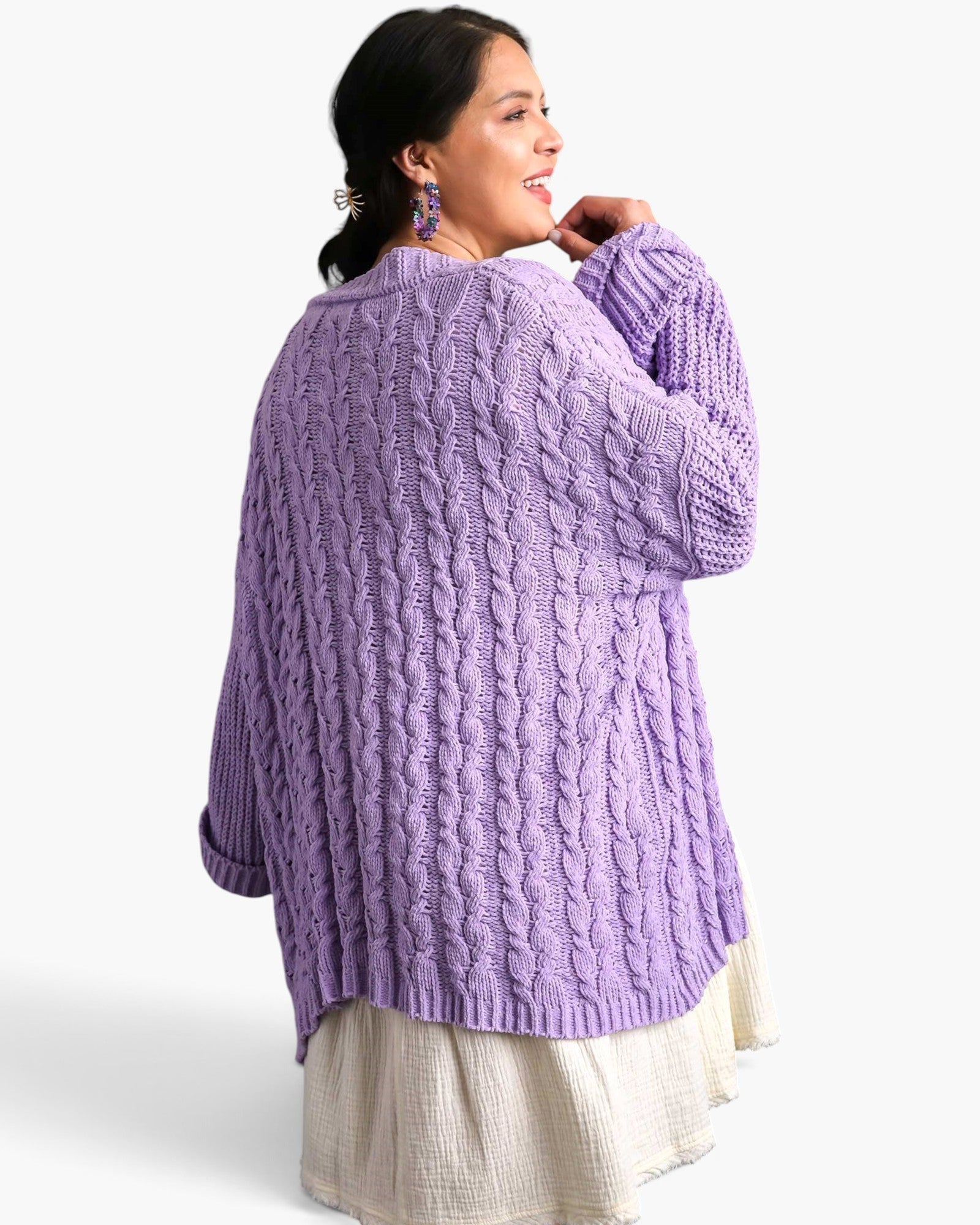 A woman wearing a chunky cable-knit lavender sweater, shown from the back and side against a clean white studio background.