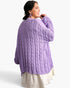 A woman wearing a chunky cable-knit lavender sweater, shown from the back and side against a clean white studio background.