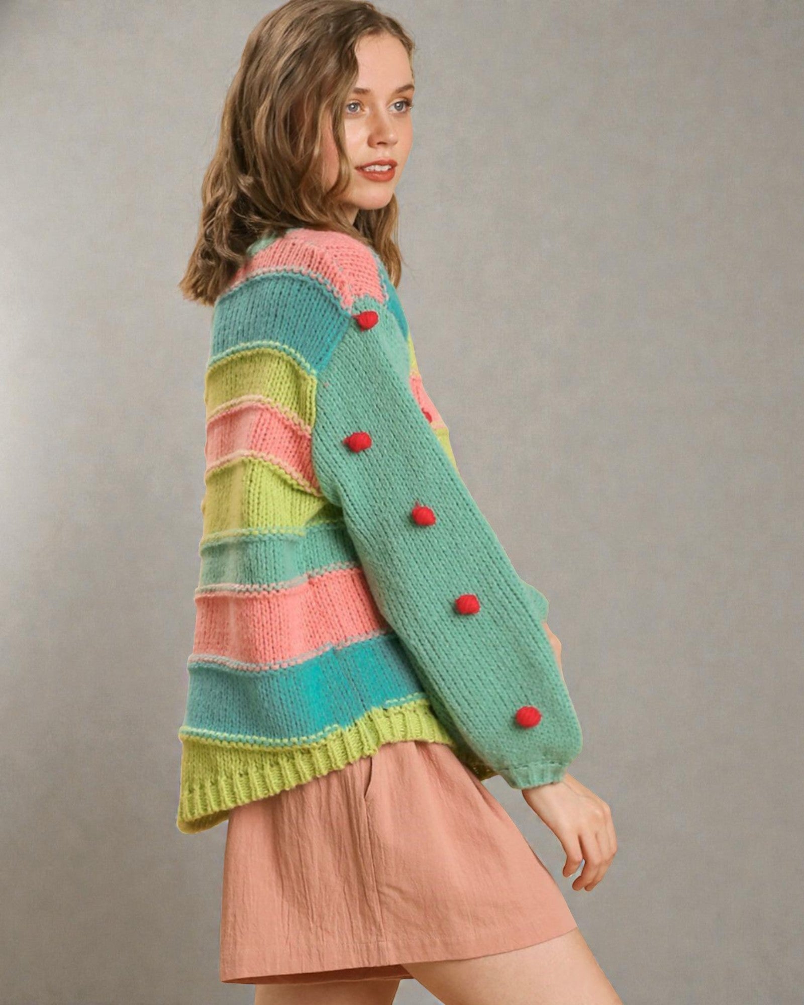 Woman wearing a colorful striped sweater with red buttons on a plain background