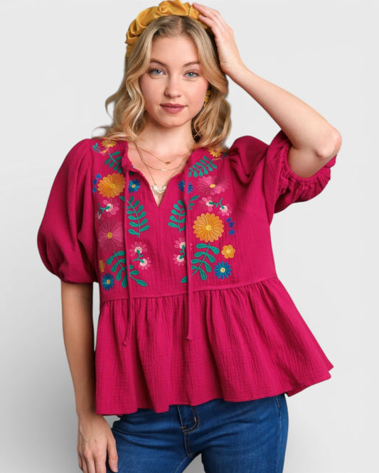 Woman wearing a pink blouse with floral embroidery on a white background