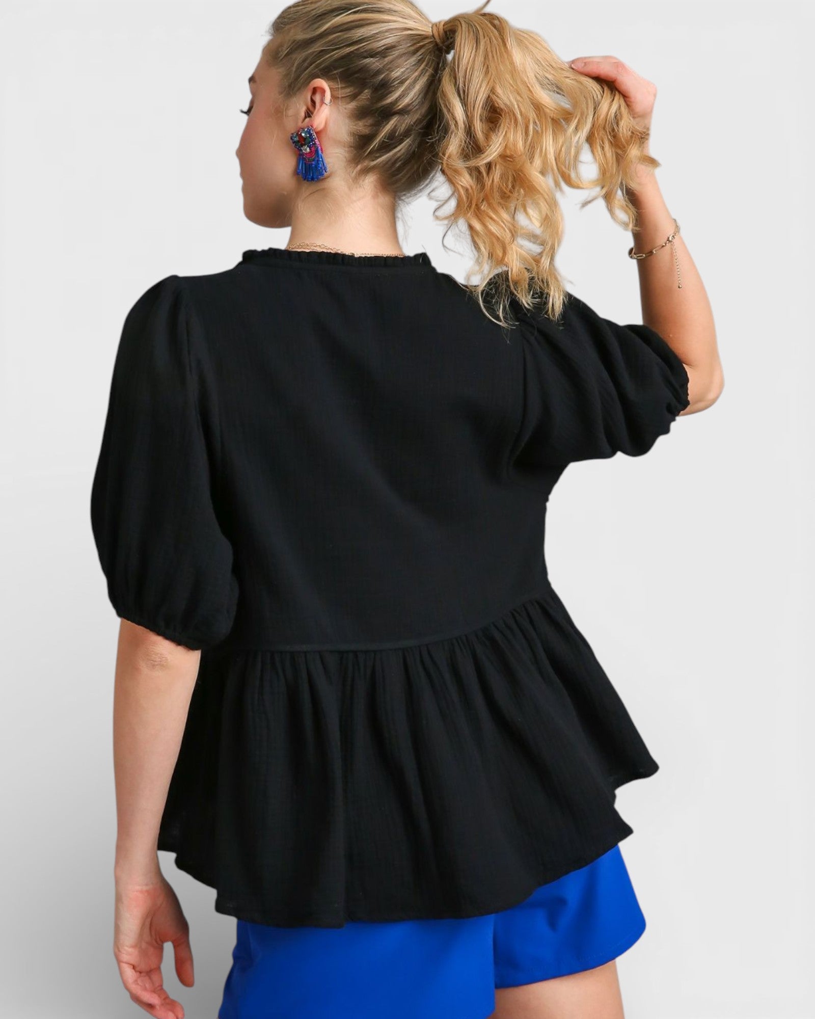 Woman wearing a black peplum top and blue shorts on a white background