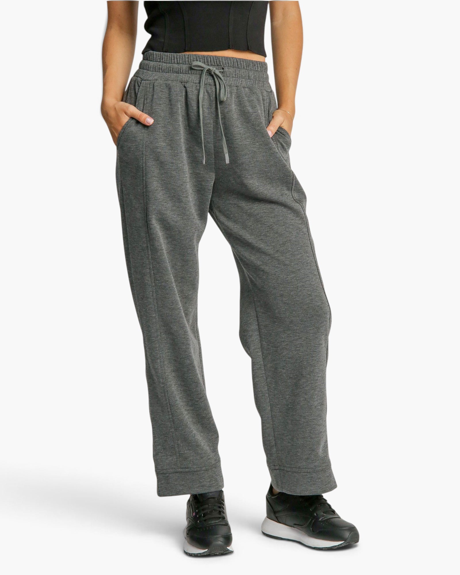 A person wearing heather gray drawstring sweatpants with side pockets, paired with black sneakers, shown from the waist down against a light gray studio background.