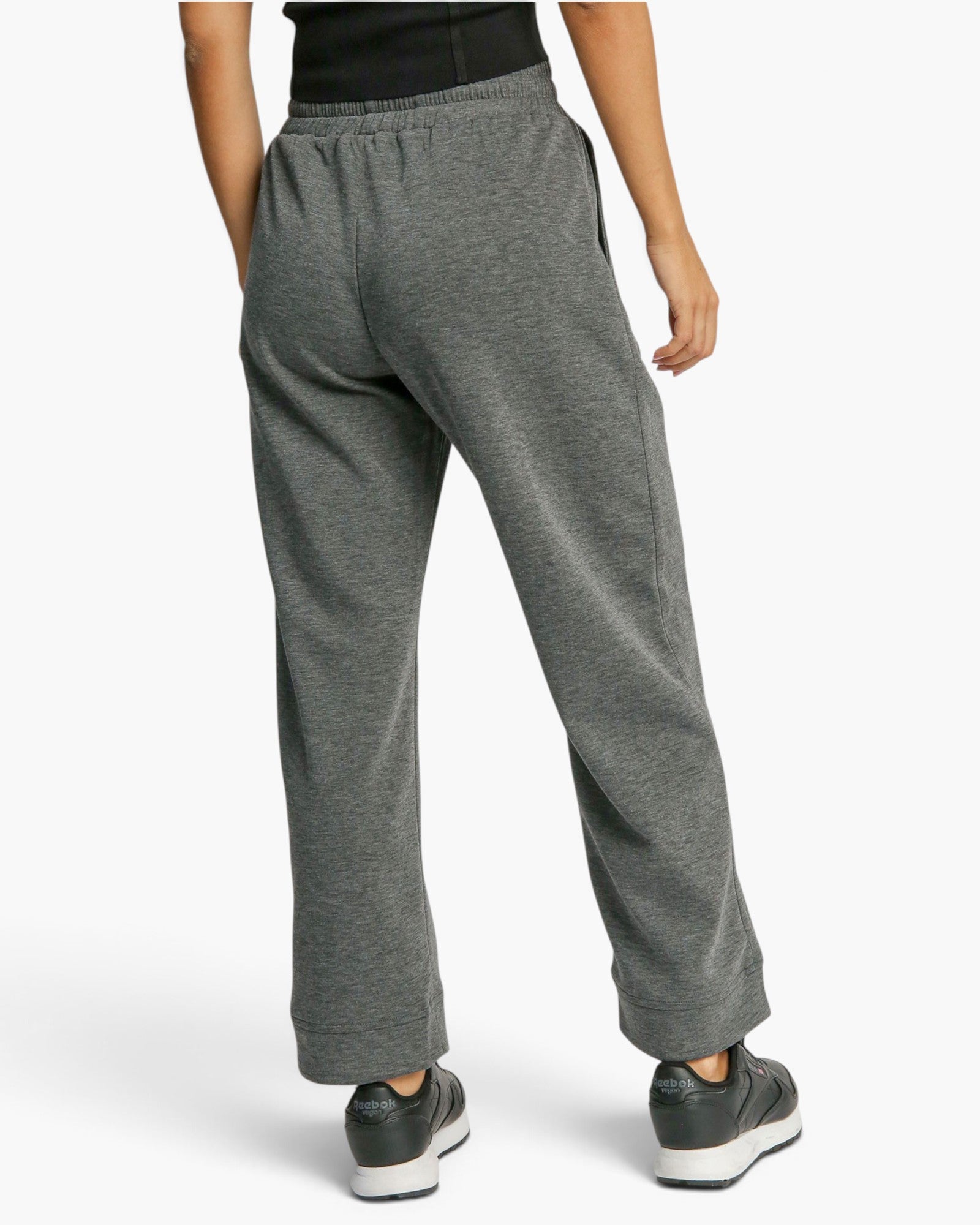 A person shown from the back wearing heather gray lounge pants, a black top, and dark sneakers against a clean light gray studio background.
