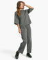 A woman modeling a dark gray heathered lounge set consisting of a cropped short-sleeve top and matching drawstring sweatpants, paired with black sneakers, against a light gray studio background.
