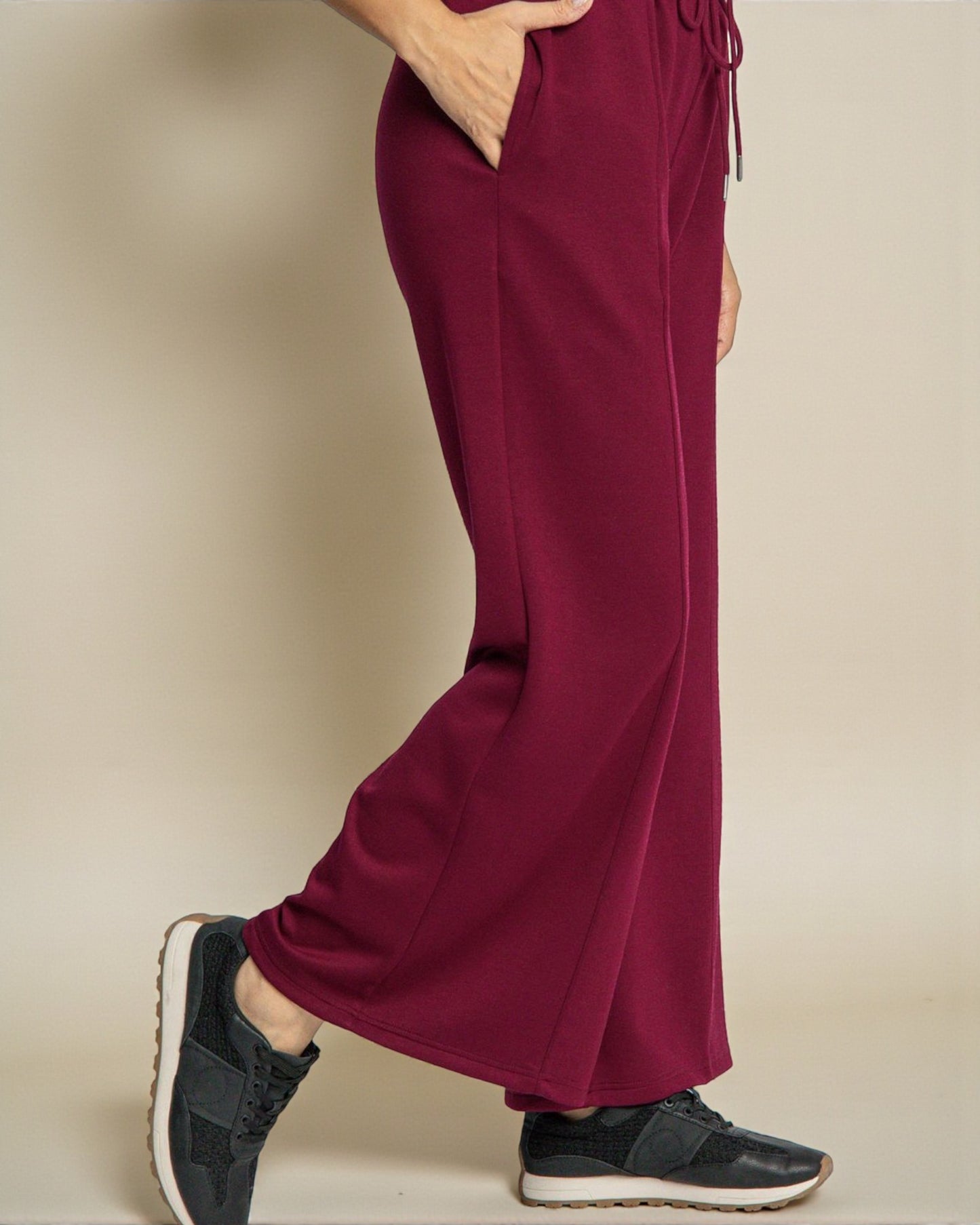 Maroon sweatpants worn by a person on a beige background