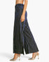 A model is shown from the waist down wearing wide-leg trousers with vertical metallic silver stripes on a dark navy blue velvet-like fabric, paired with metallic silver slingback heels, against a plain white background.