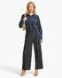 A woman modeling a matching two-piece jumpsuit set featuring a blue and black vertically striped velvet fabric. The set includes a long-sleeve collared button-up shirt and matching wide-leg pants.