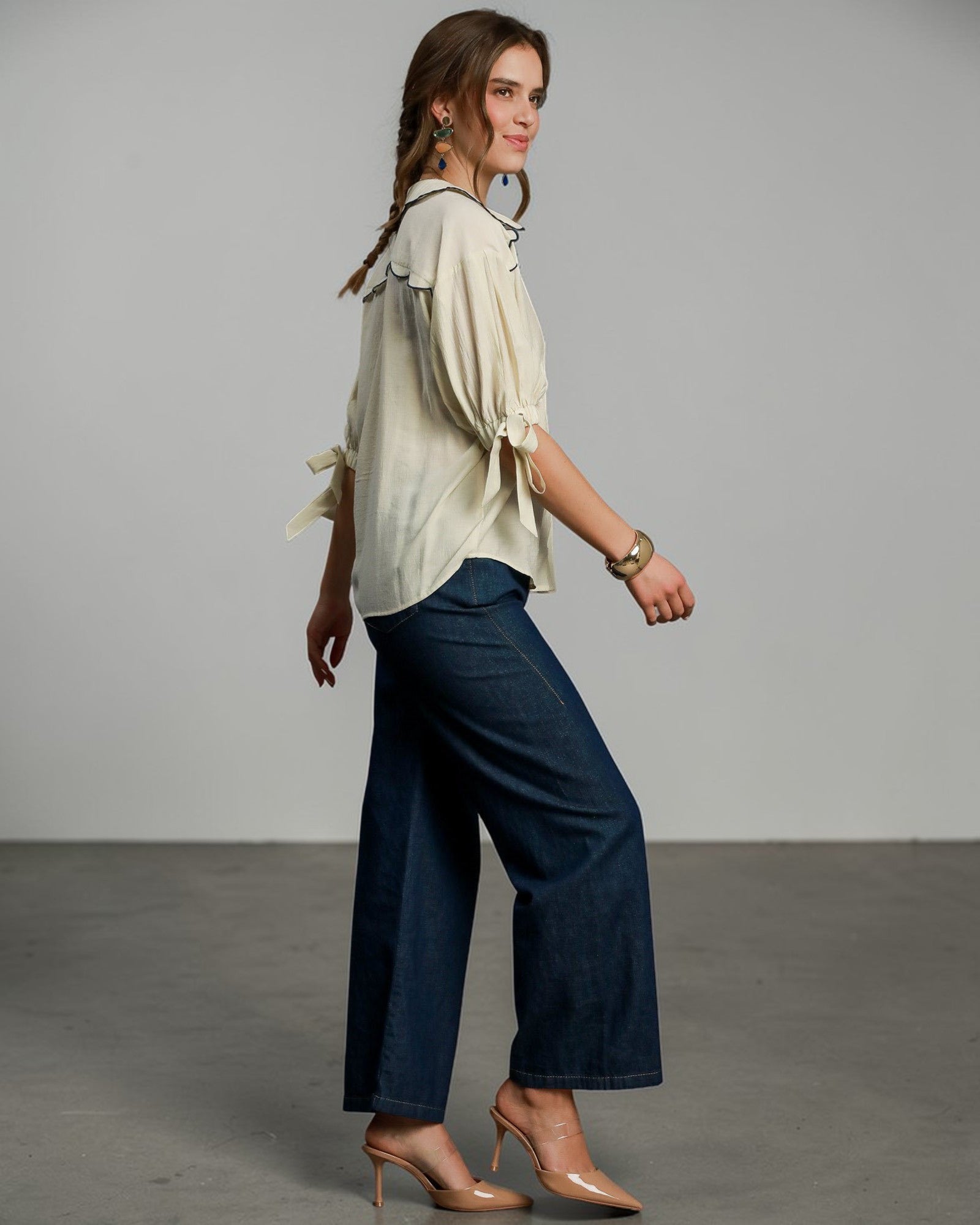 Woman wearing a light blouse and dark blue pants against a gray background