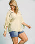 Woman wearing a light-colored blouse with black trim and denim shorts on a plain background