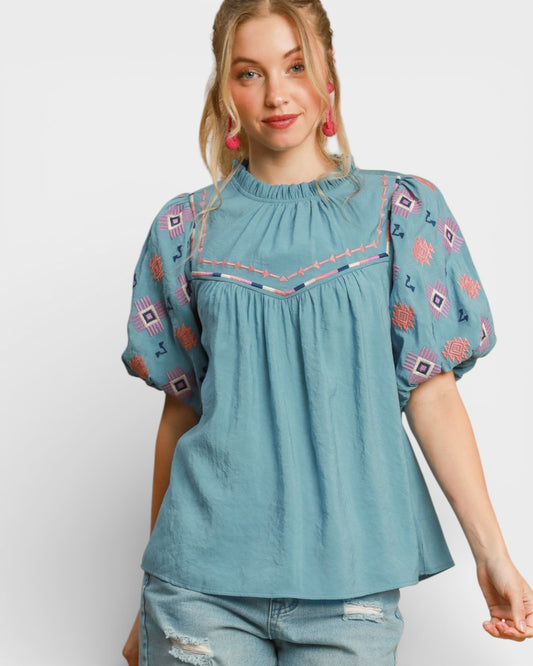 Woman wearing a blue embroidered blouse with a plain background