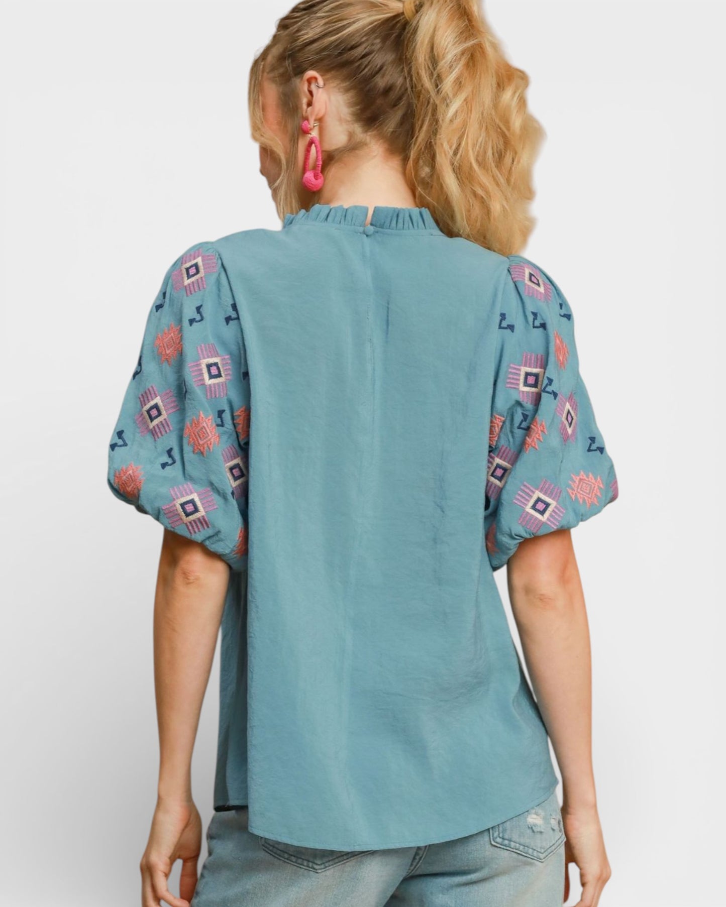 Woman wearing a teal blouse with patterned sleeves on a white background