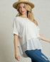 Woman wearing a white layered top and blue jeans with a straw hat on a neutral background