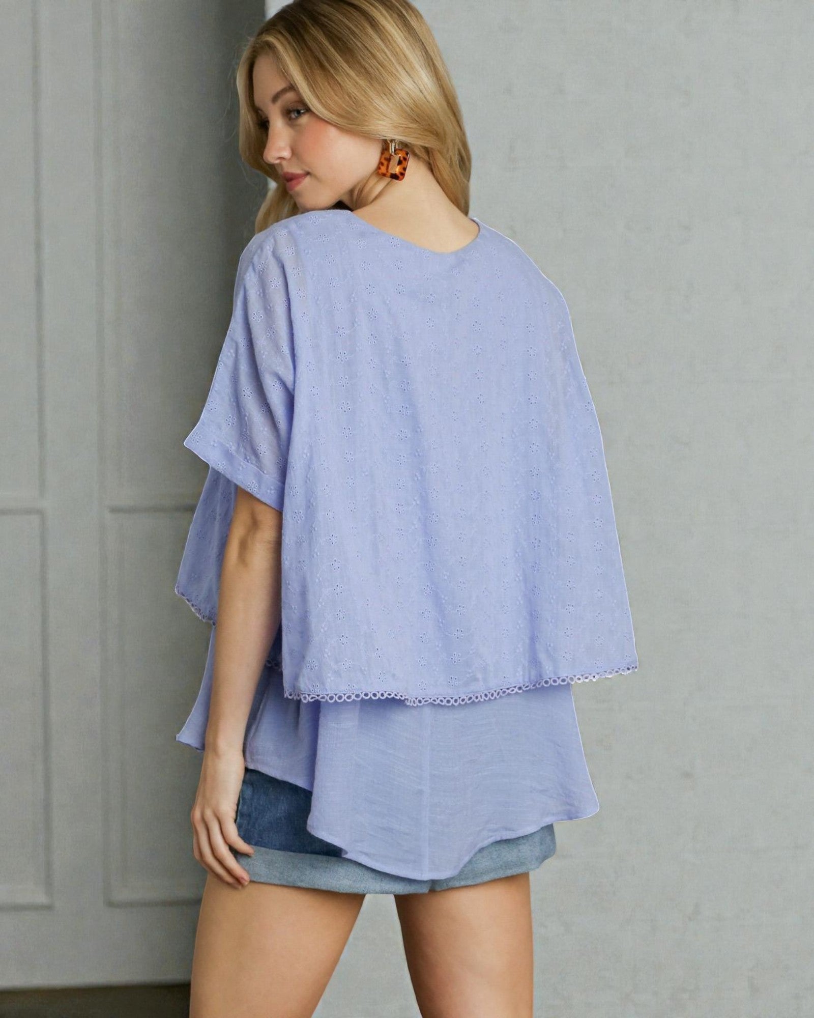 Woman wearing a light blue layered top and denim shorts against a gray background