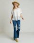Woman wearing a white top and blue jeans with a straw hat on a plain background