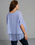 Woman wearing a light blue layered top against a gray background