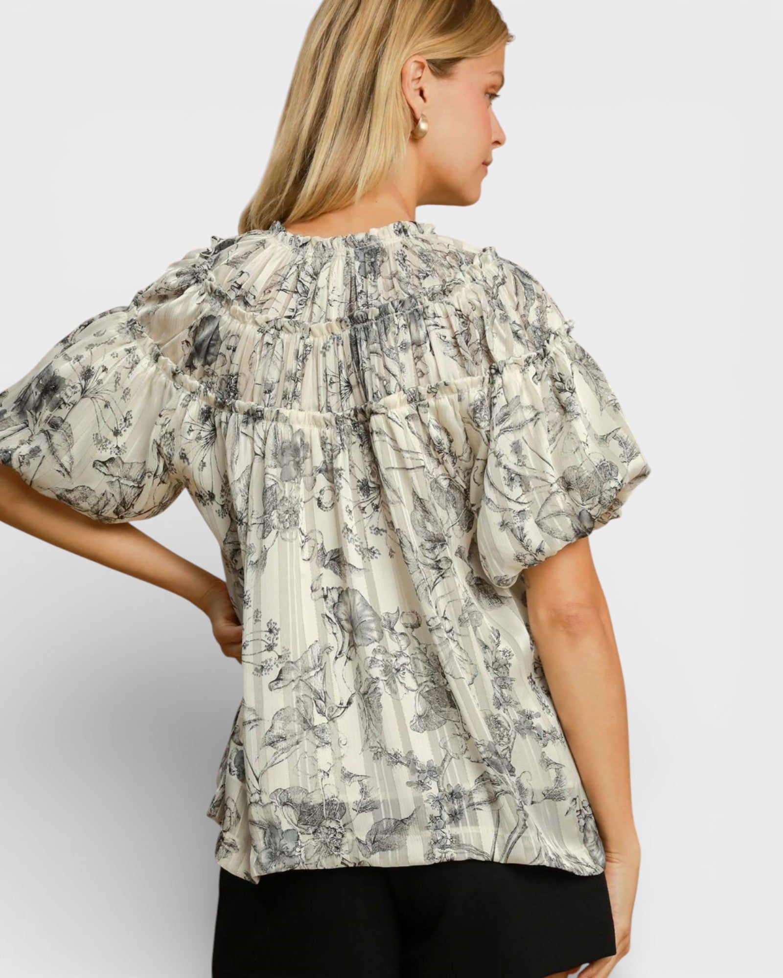 Woman wearing a floral blouse with puffed sleeves on a plain background
