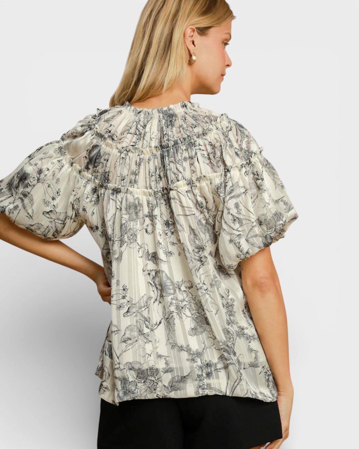 Woman wearing a floral blouse with puffed sleeves on a plain background