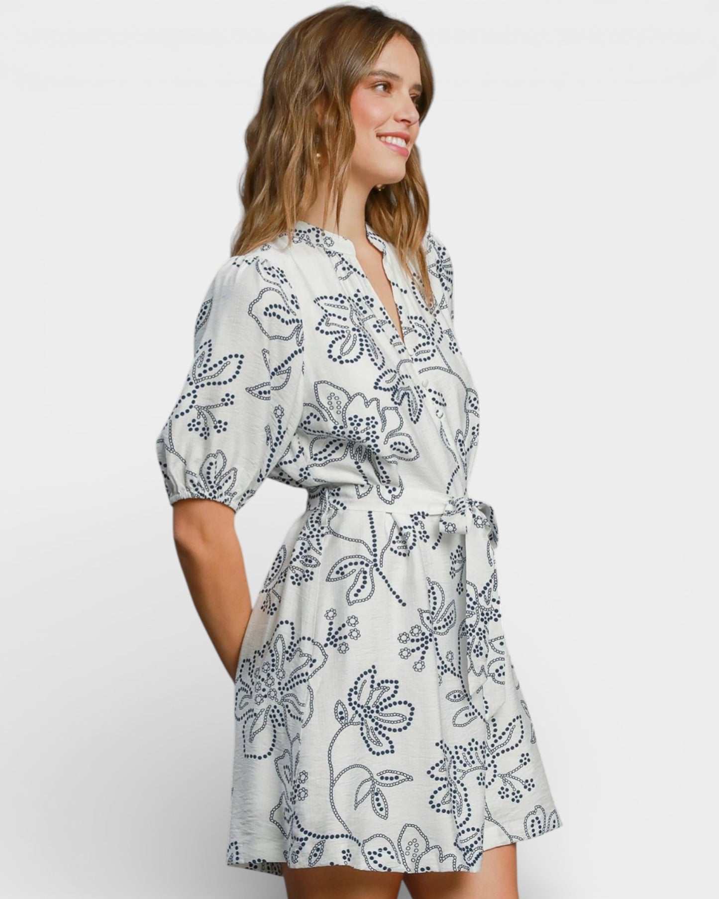 Woman wearing a white dress with black floral pattern on a plain background