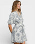 Woman wearing a white dress with black floral pattern on a plain background