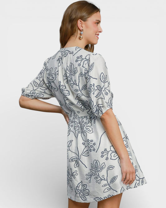 Woman wearing a white dress with black floral pattern on a plain background