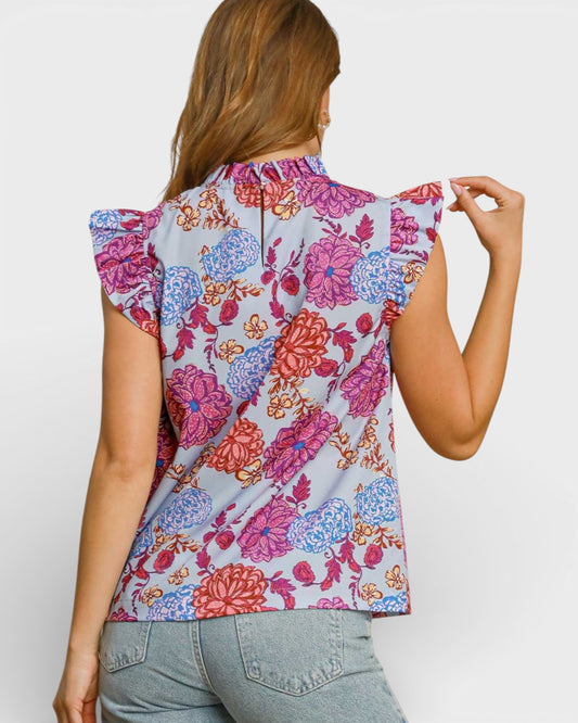 Woman wearing a sleeveless floral top with ruffled shoulders on a white background