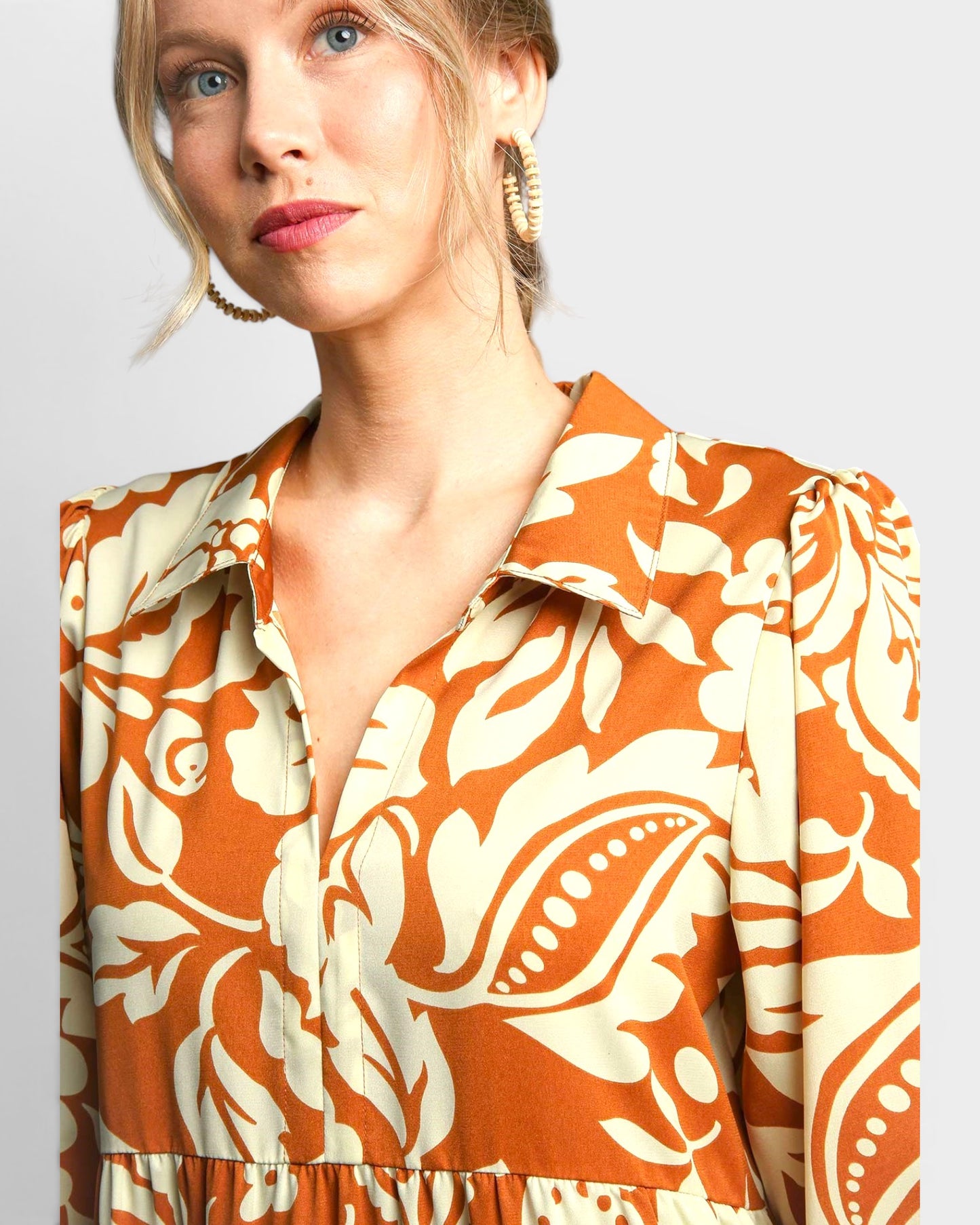 Woman wearing a patterned dress with orange and white design on a plain background