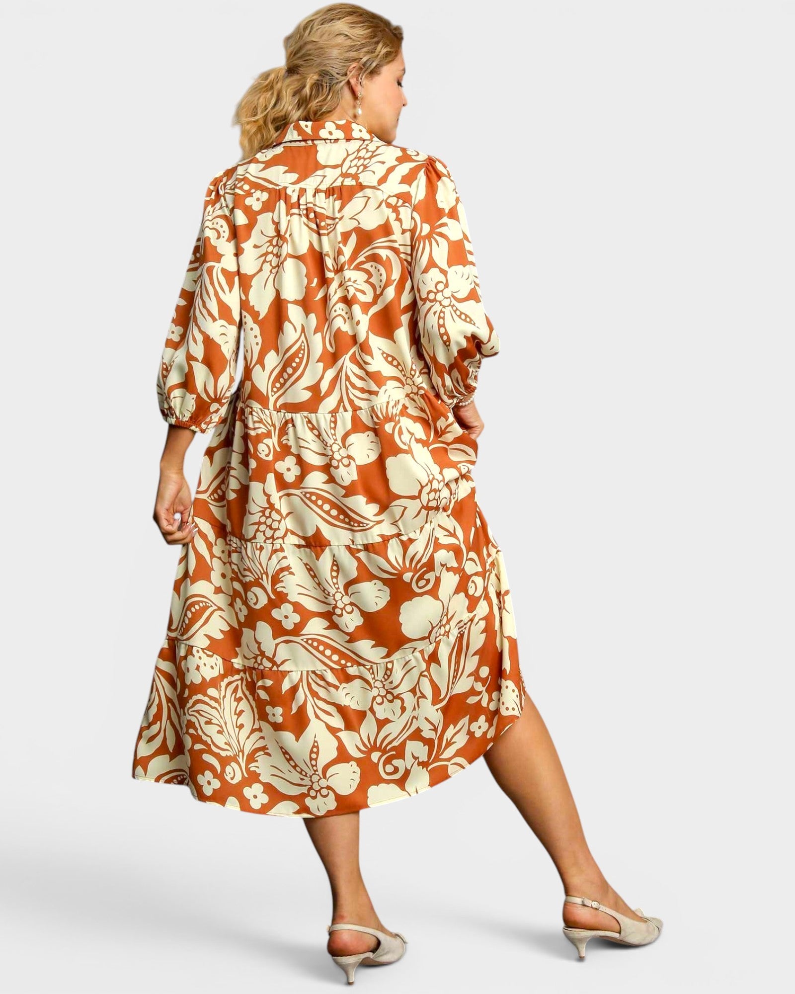 Woman wearing a long, patterned dress with orange and white design on a plain background