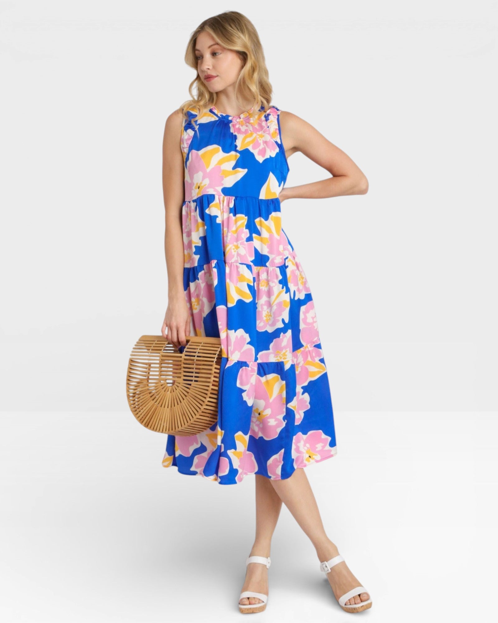 Woman wearing a blue floral dress holding a woven bag on a white background