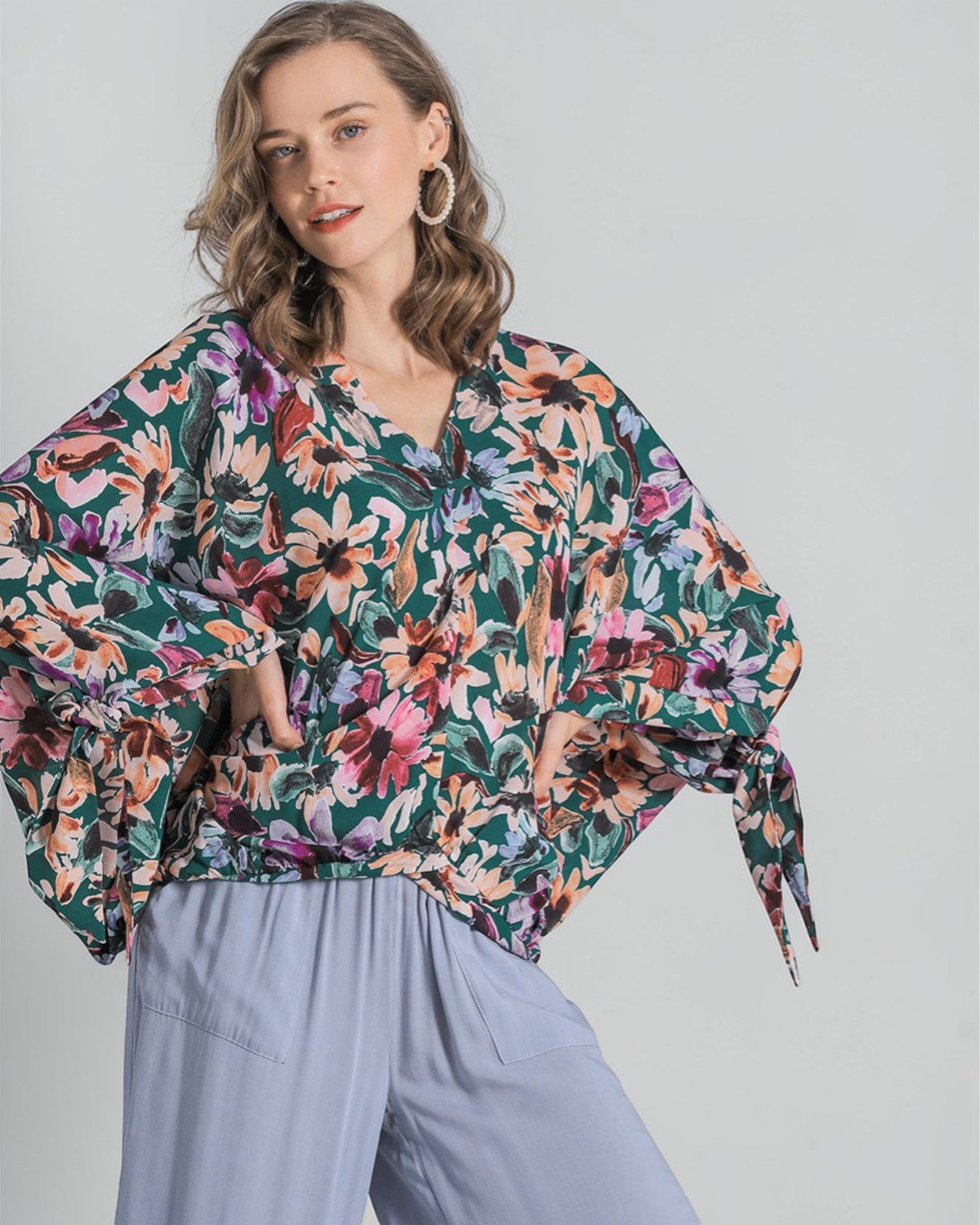 Woman wearing a colorful floral blouse with light blue pants on a plain background