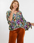 Woman wearing a colorful floral blouse and brown pants on a white background