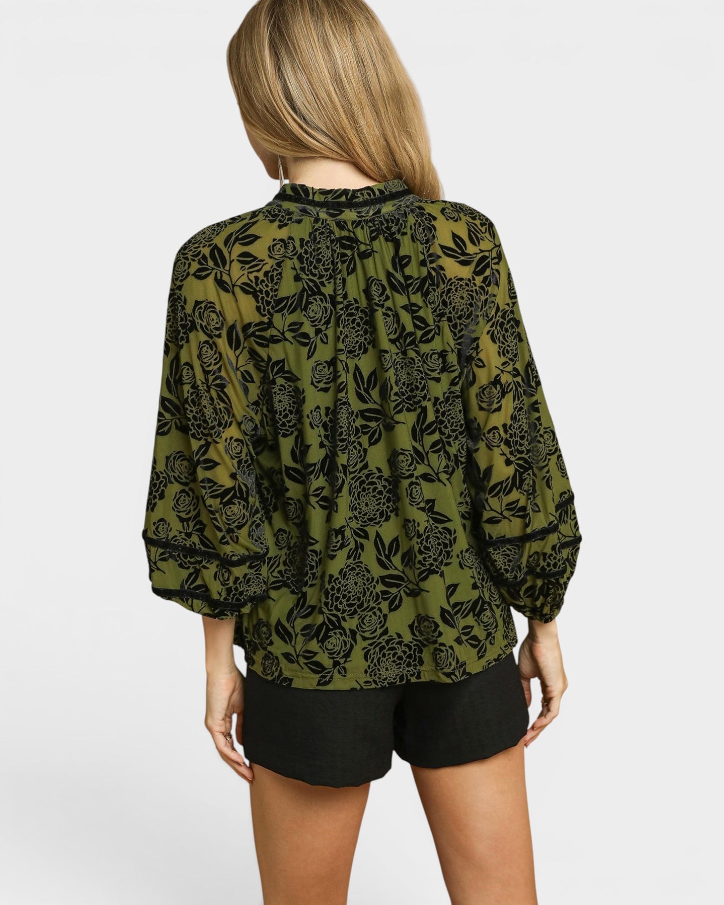 Person wearing a green patterned blouse and black shorts on a white background