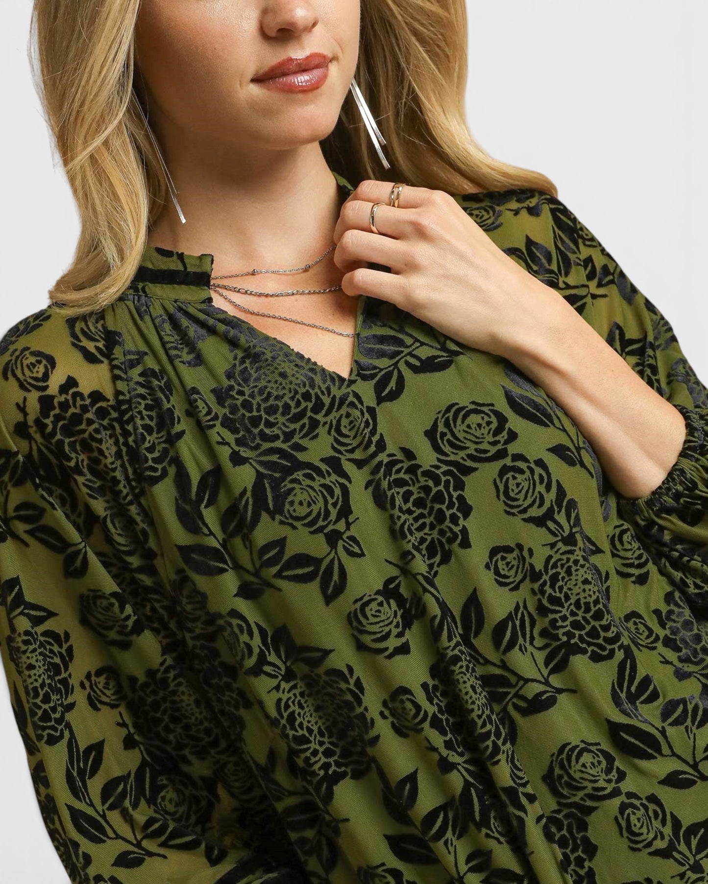 Woman wearing a green floral patterned top with a plain background